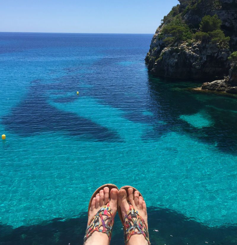 feet dangling near cliff Cala Macarelleta menorca spain